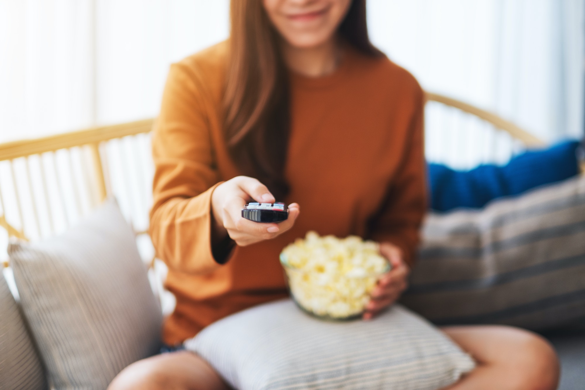 a woman eating pop corn and searching channel with remote control to watch tv