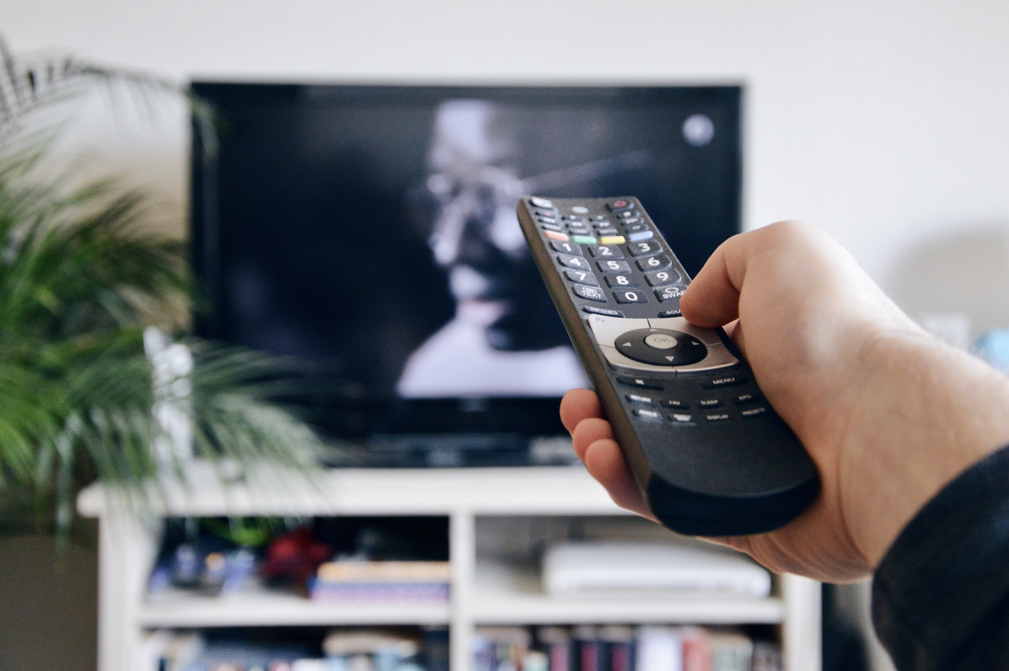 A person holding a remote control to switch channel on tv